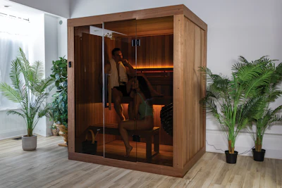 Modern wooden infrared sauna cabin with glass door in wellness room with potted plants