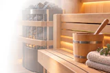 Luxury spa interior with wooden sauna, heated rocks, ambient lighting, rolled towels, and decorative plants