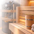 Luxury spa interior with wooden sauna, heated rocks, ambient lighting, rolled towels, and decorative plants
