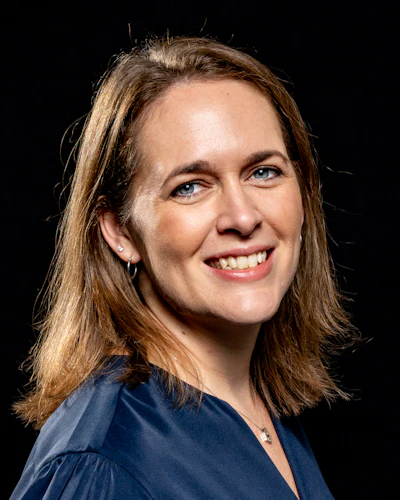 Professional headshot of a smiling woman with shoulder-length brown hair wearing a dark blue top