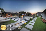Luxury modern home with illuminated pool and manicured lawn at dusk, featuring HIA 2026 Gold Award of Excellence badge