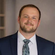 Professional headshot of a man in navy blazer and patterned tie smiling at camera