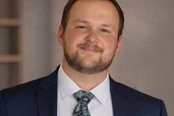 Professional headshot of a man in navy blazer and patterned tie smiling at camera