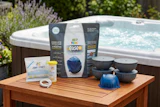 Hot tub maintenance product kit displayed on wooden table with spa in background and garden landscaping