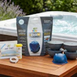 Hot tub maintenance product kit displayed on wooden table with spa in background and garden landscaping
