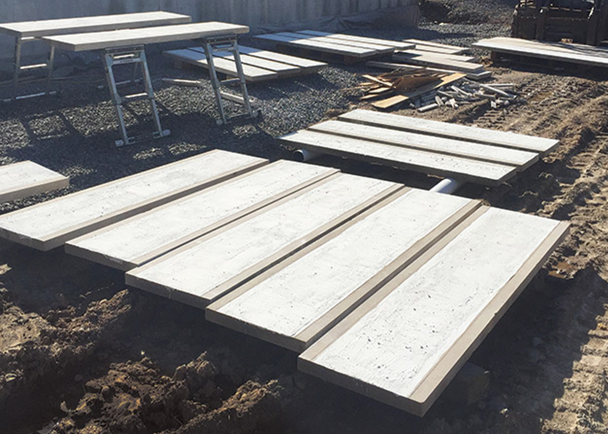 Construction site with white concrete panels and wooden frames arranged on dirt ground
