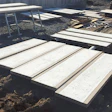 Construction site with white concrete panels and wooden frames arranged on dirt ground