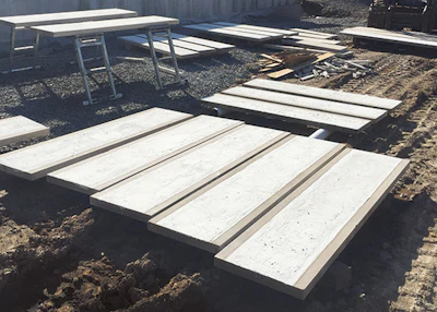 Construction site with white concrete panels and wooden frames arranged on dirt ground