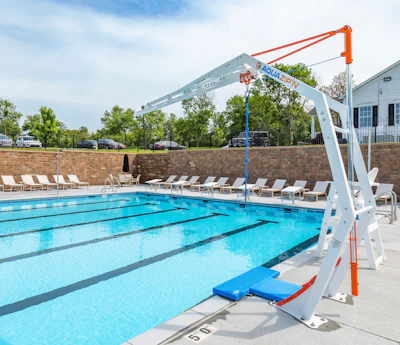 Olympic-sized swimming pool with lane dividers, white lounge chairs, brick wall, and white pool lift crane with orange accents