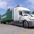 White Freightliner semi-truck with green Russin branded trailer parked in lot with trees