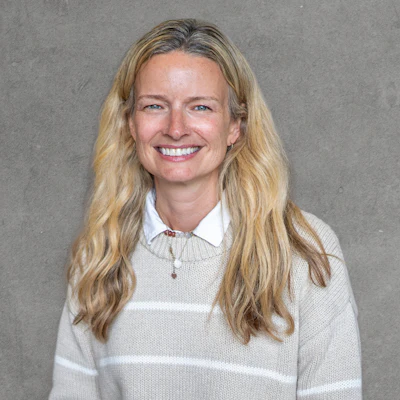 Professional headshot of a smiling woman with long blonde hair wearing a white collared sweater