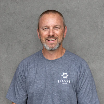 Smiling man wearing SOAKA Pools branded t-shirt against gray background